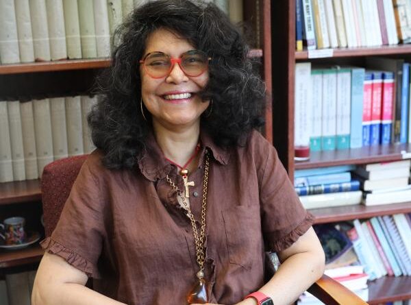 Ramona Hernández sentada frente a una biblioteca